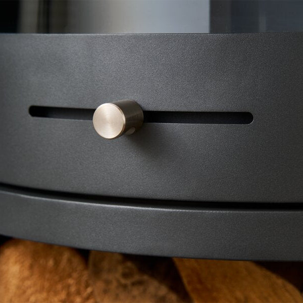 Close-up of a dark charcoal gray circular bioethanol stove highlighting the  artificial air knob and a horizontal slot detail, with logs visible below.