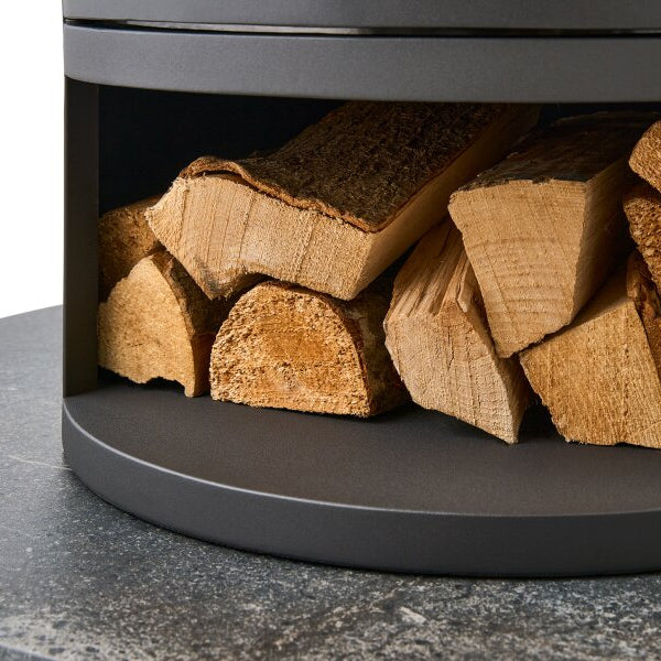 Close-up of a dark charcoal gray bio ethanol  oko S5 stove with firewood logs stacked inside, set on a speckled gray stone Lava finish semi circular hearth surface.