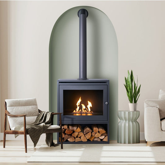 Image of an S6 on a log store with flue piope; A tall grey tube made of metal that sits ontop of a grey box like structure made of steel that has a metal chamber inside that houses BIOETHANOL fuel and you ignite and it produces heat. A 100% eco friendly renewable energy resource that's been turned into liquid. This is put into the metal chamber inside the fire box and lite to produce real flames and real heat and no chimney is required. 